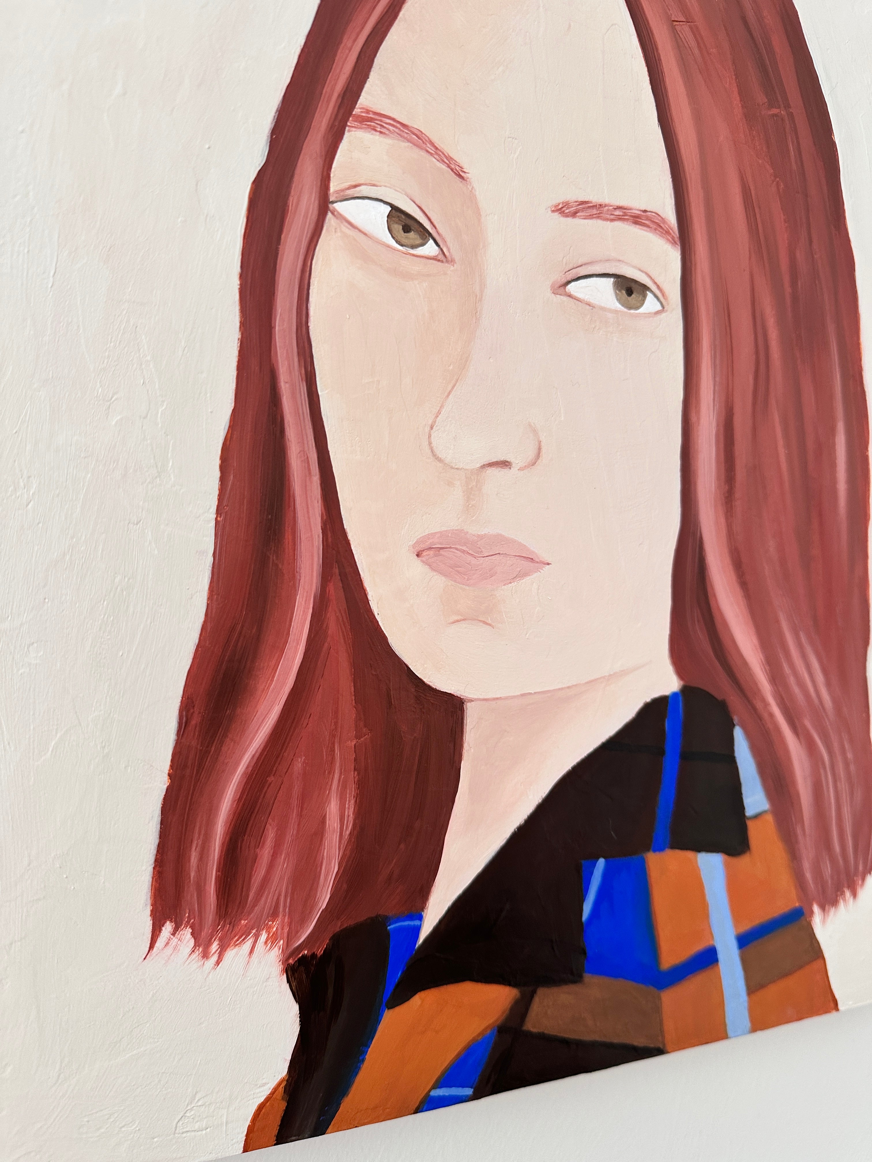 A close-up portrait painting of a woman with shoulder-length reddish-brown hair, pale skin, and a black, orange, and blue patterned top, shown against an off-white textured background.